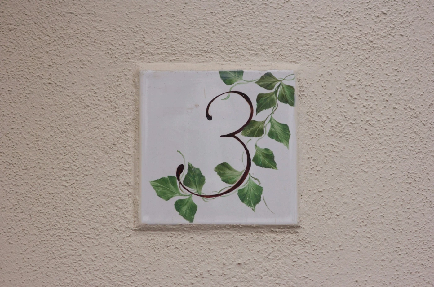 生成りの壁に掲げられた、数字の3と緑の葉が描かれたプレート